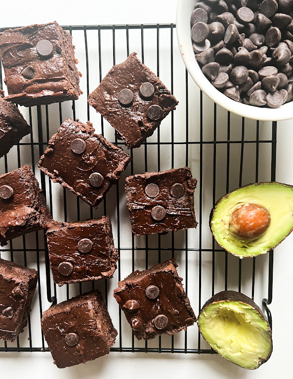 Brownies au chocolat sur une grille de refroidissement, garnis de pépites de chocolat, avec un avocat coupé à côté.