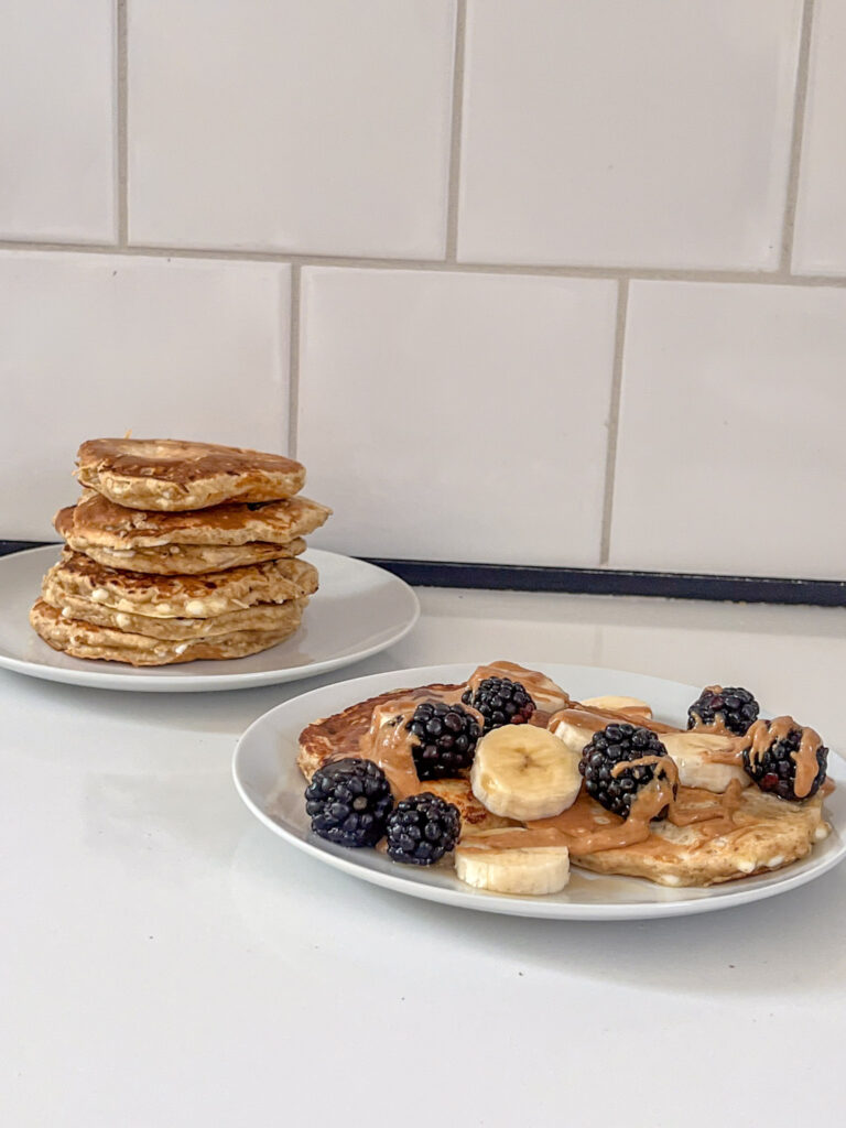 Assiette de pancakes avec des bananes et des mûres, accompagnée de beurre de cacahuète.