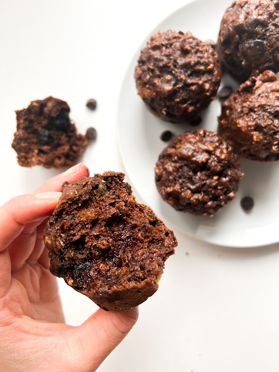 Un muffin au chocolat coupé en deux, tenu dans une main, avec d'autres muffins au chocolat en arrière-plan sur une assiette.