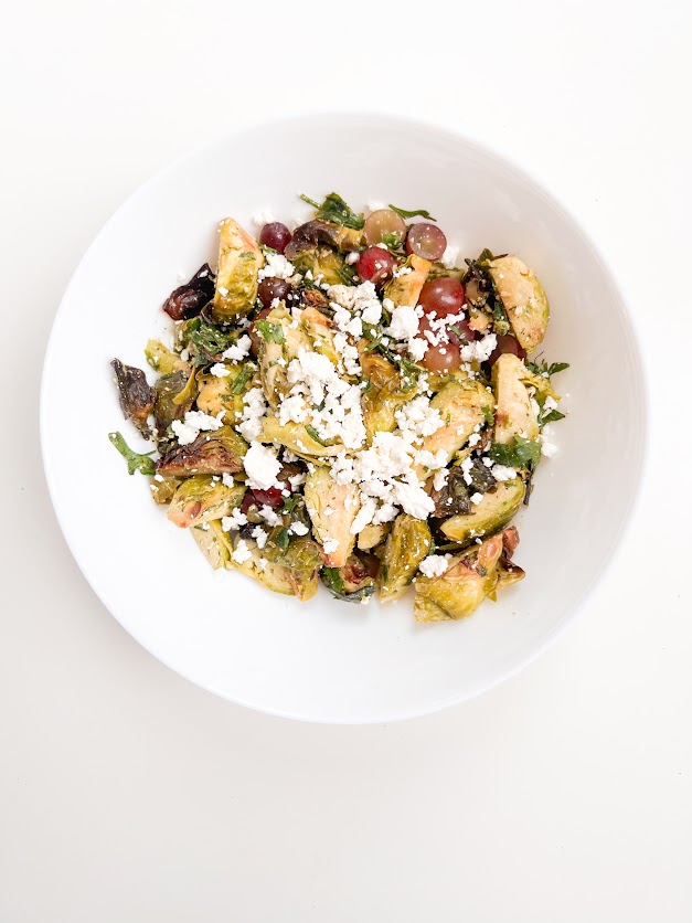 Salade de choux de Bruxelles grillés avec feta, raisins et épinards, servie dans un bol blanc.