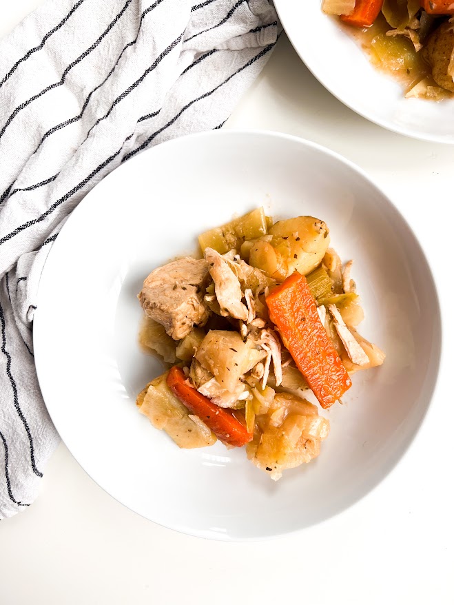 Un plat composé de morceaux de poulet, de pommes de terre, de carottes, de céleri et d'autres légumes, servi dans une assiette blanche.