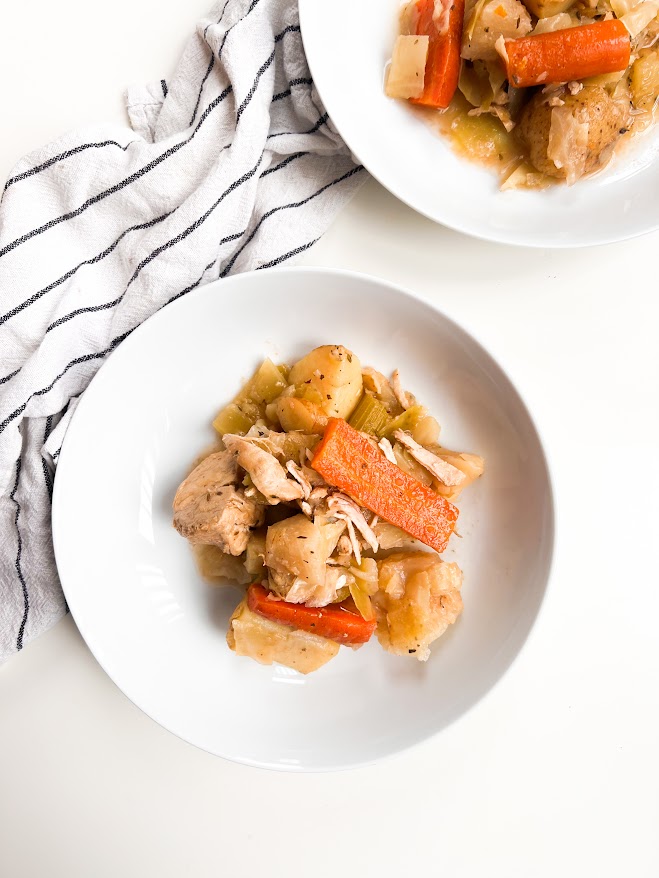Un bol de bouilli de poulet et légumes, incluant des morceaux de carottes, céleri et pommes de terre, servi sur une nappe rayée.