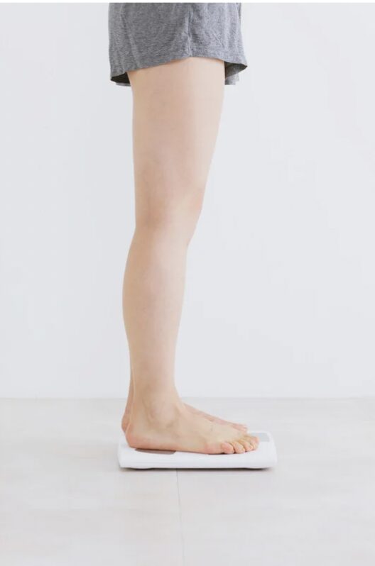 Une personne se tient sur une balance blanche, visible du côté droit de la photo, avec une jambe et un pied nus.