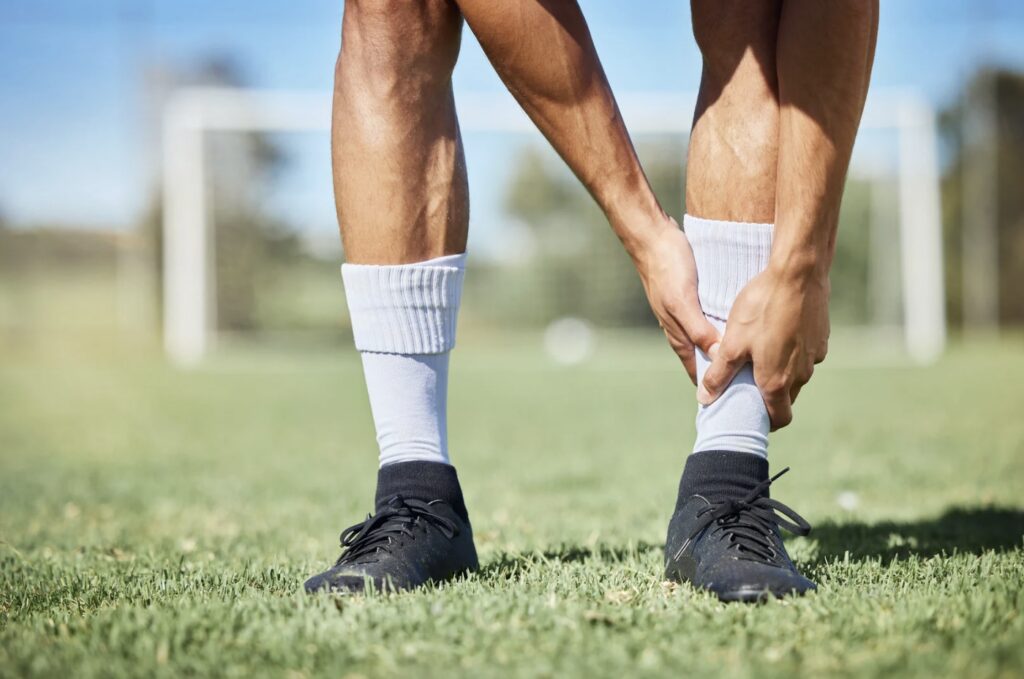 Un athlète ajuste ses chaussettes sur un terrain de sport, mettant l'accent sur ses jambes musclées et ses chaussures de football.