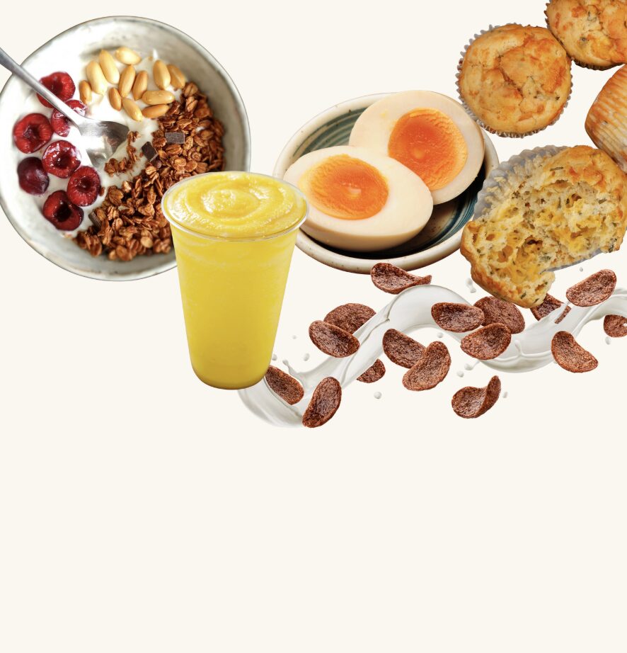 Un assortiment de collations saines comprenant un bol de granola avec des fruits rouges, un verre de smoothie jaune, des œufs durs et des muffins, avec des céréales disposées artistiquement.