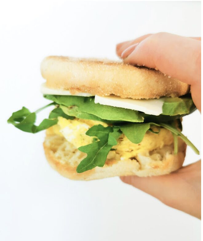 Sandwich avec un œuf, des épinards et du fromage dans un pain anglais, tenu à la main.