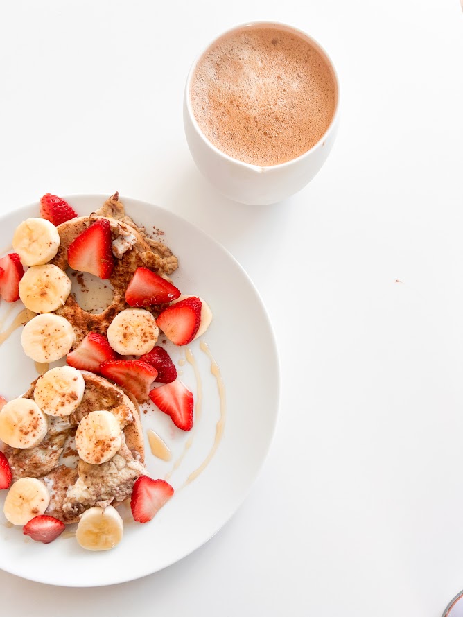 Assiette de crêpes garnie de tranches de banane et de fraises, accompagnée d'une tasse de café.